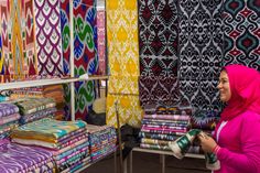 a woman is looking at fabrics on display in a market area with colorful colors and patterns