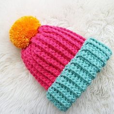 a crocheted hat with a pom - pom sits on a fluffy white surface