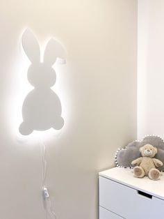 a teddy bear sitting on top of a white dresser next to a bunny shaped light