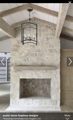 an empty room with a stone fireplace and wood flooring on the walls, along with a chandelier hanging from the ceiling