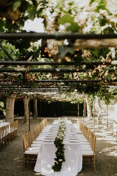 a long table with white linens and greenery is set up for an outdoor wedding