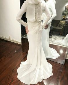 a woman standing in front of a mirror wearing a white wedding dress with long sleeves