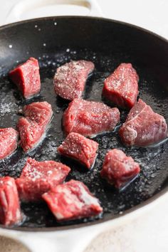 raw meat being cooked in a skillet on a stove top with oil and seasoning