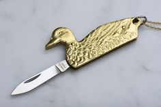 a gold duck pendant with a knife in it's mouth on a marble surface