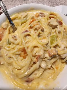 a white bowl filled with pasta and meat on top of a table next to a fork