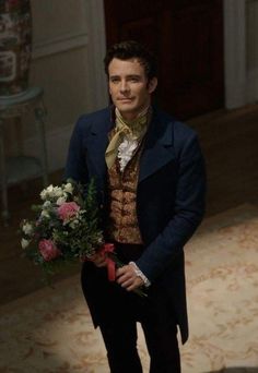 a man in a suit and bow tie holding a bouquet of flowers while standing on a carpeted floor