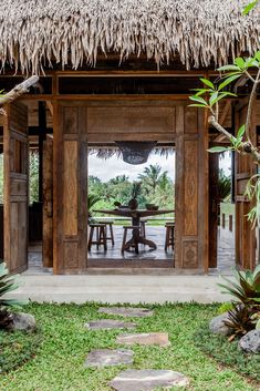 an outdoor dining area with thatched roof and wooden table surrounded by greenery on the lawn