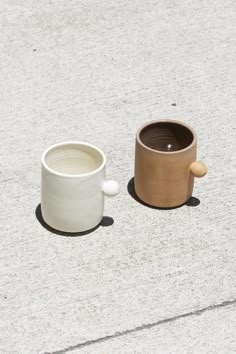 two mugs sitting on the ground next to each other, one with a spoon in it