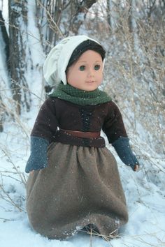 a doll is sitting in the snow wearing a brown dress and white headdress