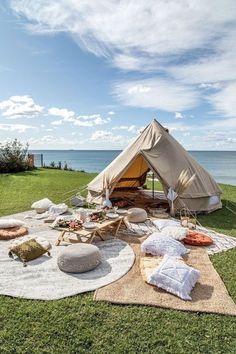 a tent is set up on the grass by the ocean with pillows and blankets around it