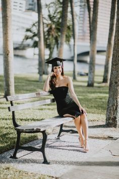 a woman sitting on top of a bench wearing a graduation gown and holding a black hat