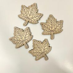 four wooden maple leaf magnets on a white surface