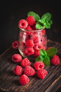 raspberries and mint leaves in a glass jar on a wooden table royalty images