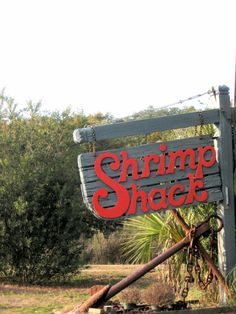 a sign that says shrimp shack hanging from the side of a building with trees in the background