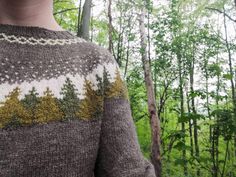 a person standing in the woods wearing a sweater with trees on it and bushes behind them