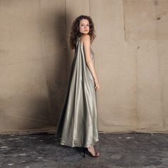 a woman standing in front of a wall wearing a silver dress