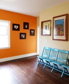 an empty room with three blue benches in front of orange walls and pictures on the wall