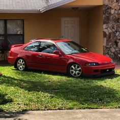 a red car parked in front of a house on the grass next to a fire hydrant