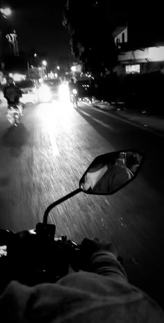 a person riding a motorcycle down a street at night with the headlights shining on them