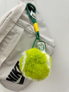 a green pom - pom keychain attached to a white backpack