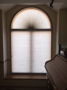 an arched window with blinds on the outside and inside, in front of a wooden bench