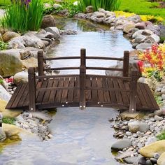 a wooden bridge over a small stream surrounded by rocks and flowers in a garden area