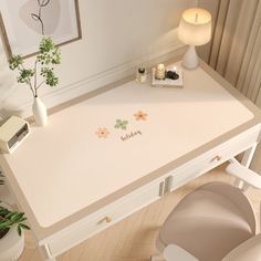 a white desk with flowers on it in a room next to a lamp and potted plant