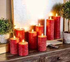 red candles sit on a dresser in front of a mirror and potted plant next to it