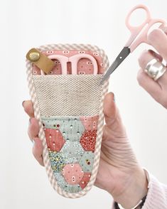 a person holding a pink scissors in a case with patchwork and hearts on it