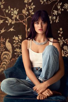 a woman with purple hair is sitting on a blue chair in front of a floral wallpaper