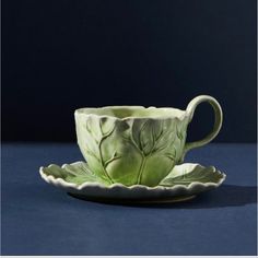 a green cup and saucer on a blue surface with the image of leaves painted on it