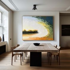 a dining room with a large painting on the wall and wooden table in front of it