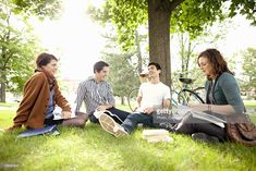 three people sitting on the grass with books in front of them and bikes behind them