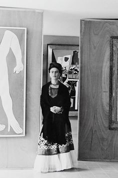 a black and white photo of a woman standing in front of a painting