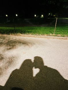 the shadow of a person holding a skateboard in front of a fence at night