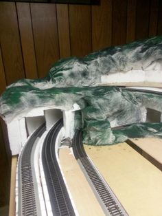 a model train track with green and white paint on it's sides, next to a wood paneled wall