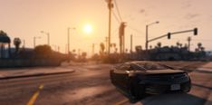 a black car driving down a street next to traffic lights and palm trees at sunset