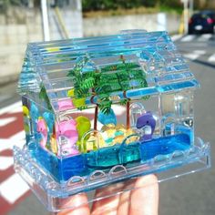 a person holding up a small toy boat in a plastic case with trees and animals inside