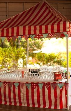 a large red and white striped tent with wine glasses on it's table under the canopy