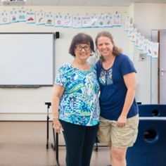 two women standing next to each other in front of a whiteboard