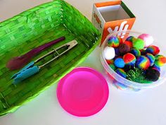 a green basket filled with pom poms next to a pink plate and scissors