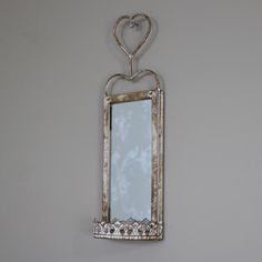 a mirror hanging on the wall with a heart shaped frame above it and an iron hook