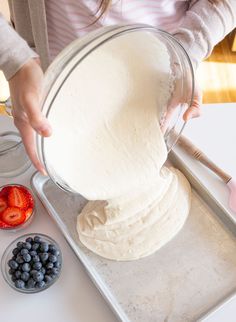 a person is making some food in a bowl on a tray with strawberries and blueberries