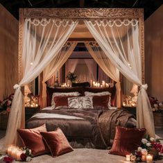 a large bed sitting under a canopy covered in white drapes next to candles and flowers