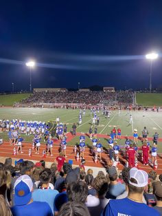 a group of people standing on top of a field next to a football field at night