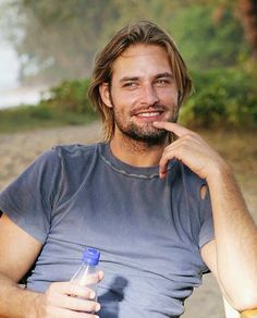 a man sitting on a beach holding a bottle and pointing to the side with his finger