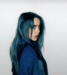 a woman with long blue hair is standing in front of a white wall and looking off to the side