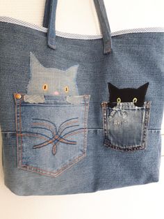 two cats are in the pocket of a denim bag that is hanging on a wall