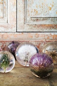 four glass vases filled with flowers on top of a wooden table next to a brick wall