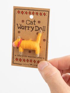 a hand holding a small yellow dog pin with the words cat worry doll on it